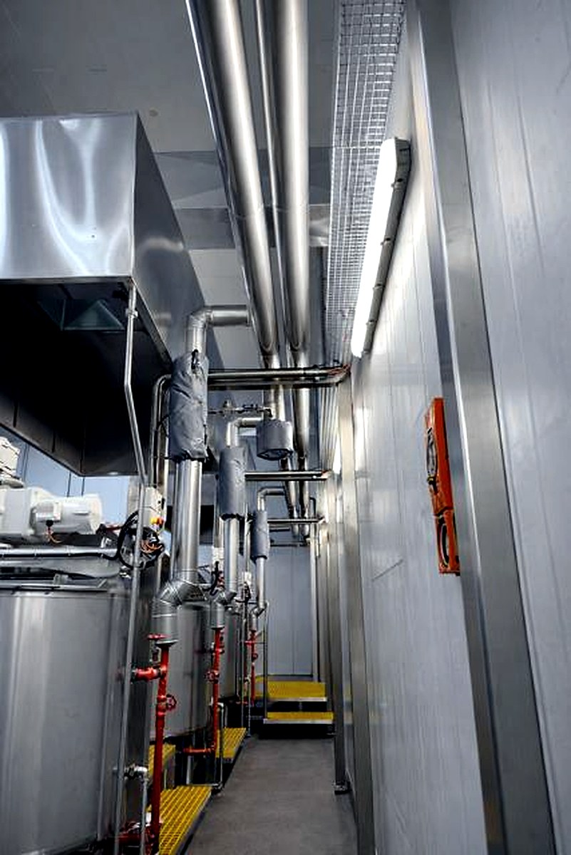 Thermal jackets on pipe fittings and connections in an industrial plant room corridor